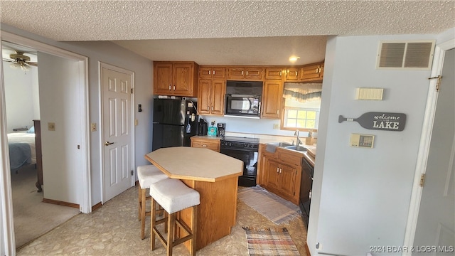 kitchen featuring a kitchen bar, a textured ceiling, ceiling fan, black appliances, and a center island