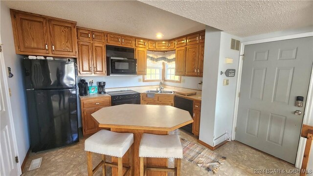 kitchen featuring a breakfast bar, black appliances, a textured ceiling, and sink