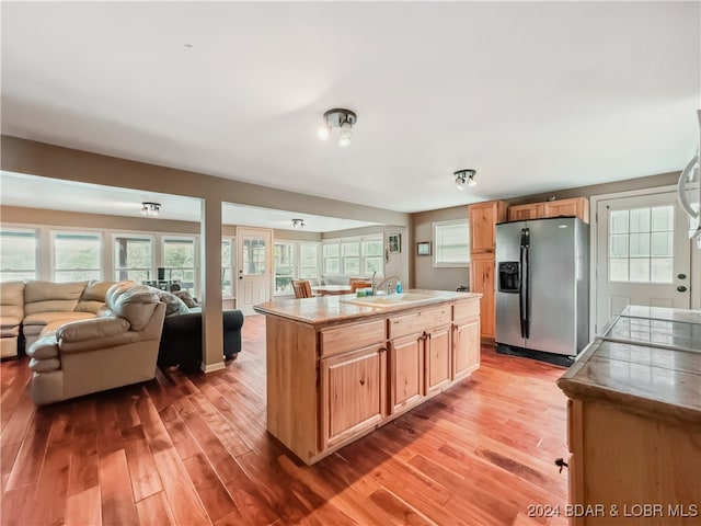 kitchen with sink, stainless steel fridge, a kitchen island with sink, and light hardwood / wood-style floors