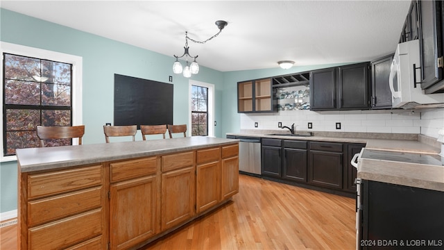 kitchen with tasteful backsplash, hanging light fixtures, stainless steel dishwasher, light hardwood / wood-style floors, and sink