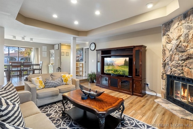 living room featuring a stone fireplace, a tray ceiling, and light wood-type flooring