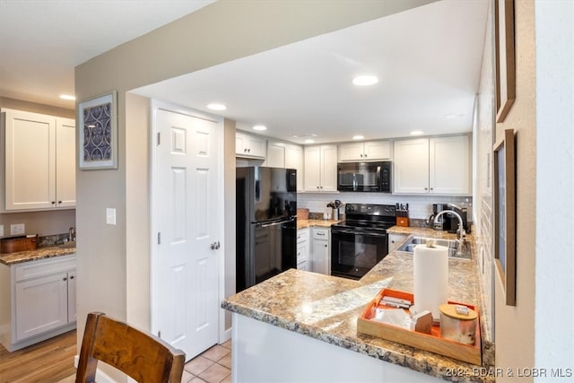 kitchen featuring kitchen peninsula, sink, black appliances, light stone countertops, and white cabinetry