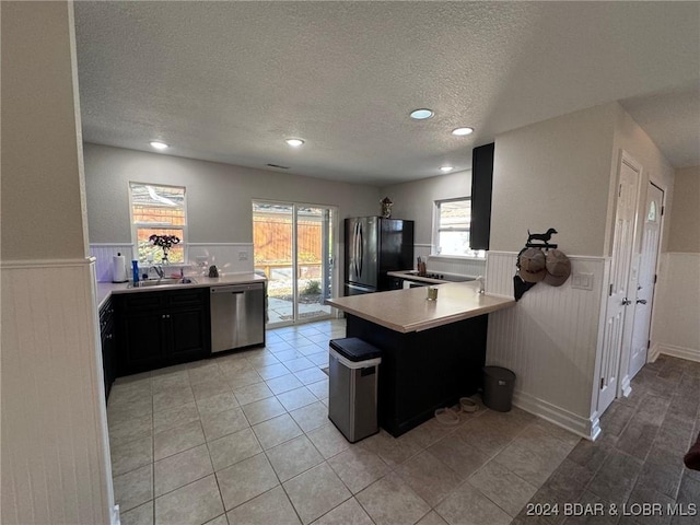 kitchen with a textured ceiling, stainless steel dishwasher, a sink, a wainscoted wall, and freestanding refrigerator