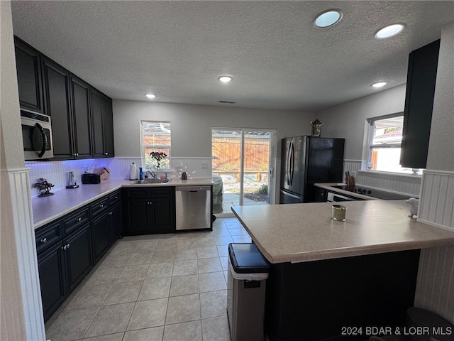 kitchen featuring kitchen peninsula, stainless steel appliances, sink, light tile patterned floors, and a textured ceiling