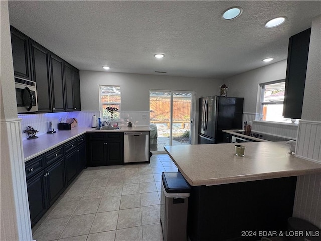 kitchen with a sink, dark cabinets, wainscoting, and stainless steel appliances