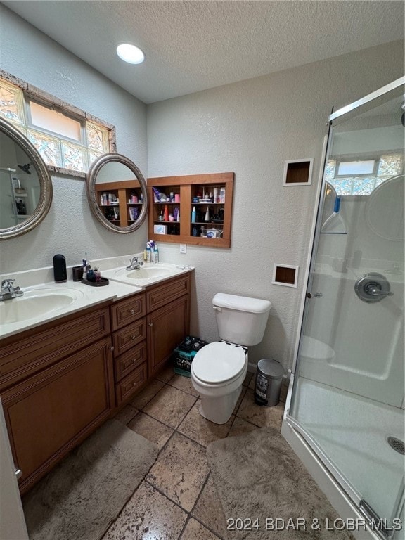 bathroom featuring vanity, toilet, a textured ceiling, and a shower with shower door