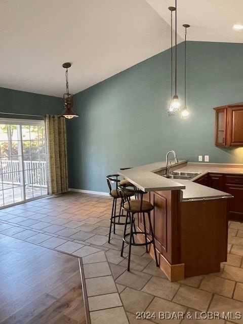 kitchen with hanging light fixtures, a breakfast bar area, vaulted ceiling, light hardwood / wood-style flooring, and sink