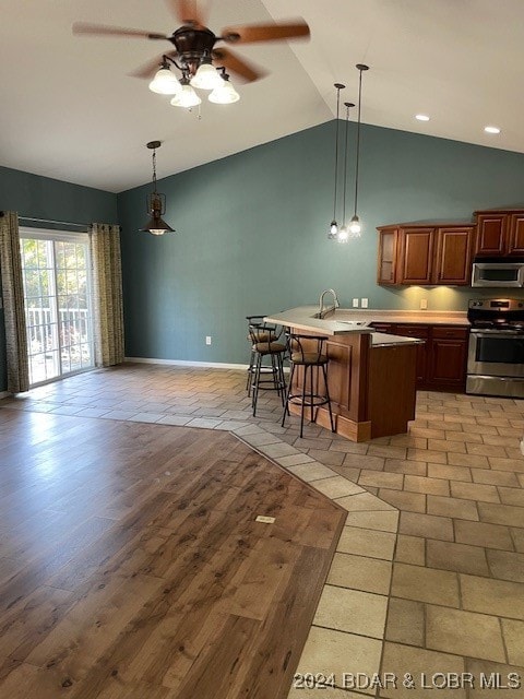 kitchen with appliances with stainless steel finishes, light wood-type flooring, hanging light fixtures, a kitchen breakfast bar, and vaulted ceiling