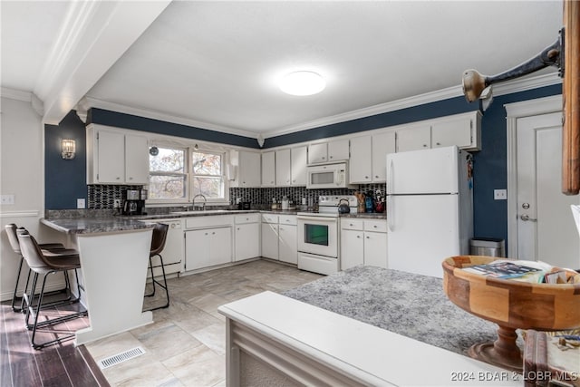 kitchen with ornamental molding, white cabinets, a kitchen bar, and white appliances