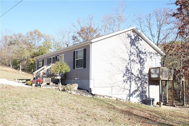 view of property exterior with a wooden deck, cooling unit, and a lawn