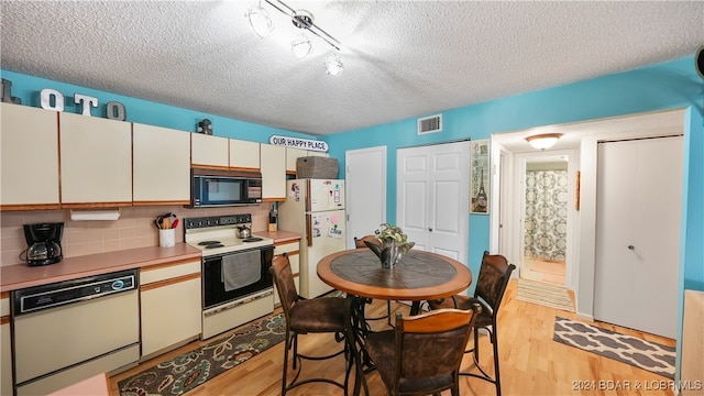 kitchen featuring white cabinets, tasteful backsplash, a textured ceiling, light wood-type flooring, and white appliances