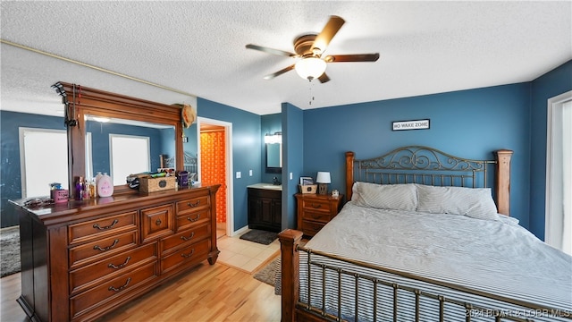 bedroom with ceiling fan, a textured ceiling, light hardwood / wood-style floors, and ensuite bath