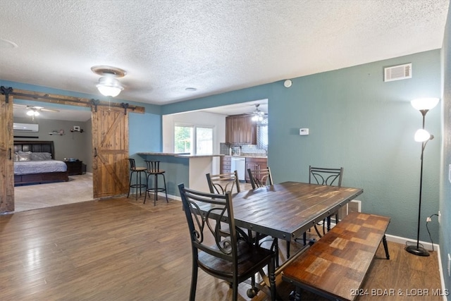 dining room featuring wood-type flooring, a textured ceiling, a barn door, ceiling fan, and an AC wall unit