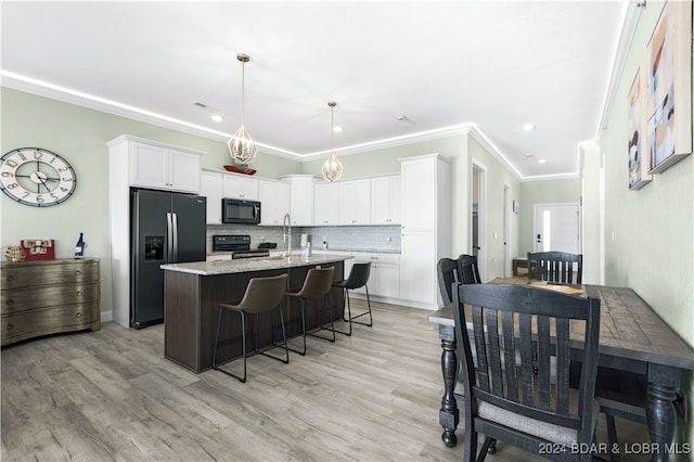 kitchen featuring black appliances, white cabinetry, light wood-type flooring, and an island with sink