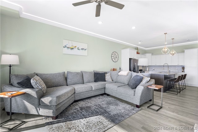 living room with light wood-type flooring, sink, ceiling fan, and crown molding