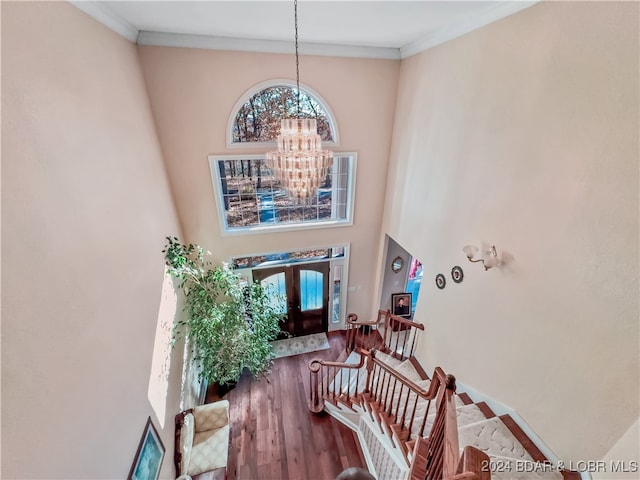 stairs featuring a towering ceiling, an inviting chandelier, ornamental molding, and wood-type flooring