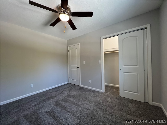 unfurnished bedroom featuring a closet, a spacious closet, a textured ceiling, dark colored carpet, and ceiling fan