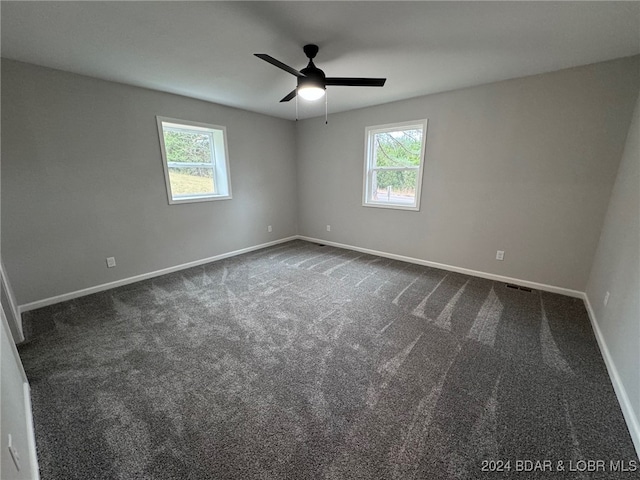 spare room with a wealth of natural light, ceiling fan, and dark carpet