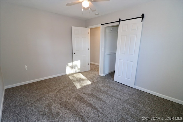 unfurnished bedroom featuring carpet flooring, a barn door, and ceiling fan