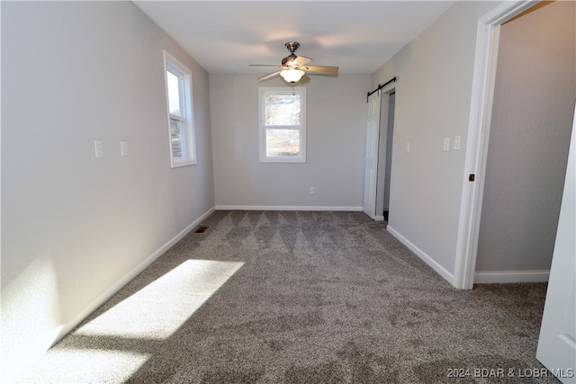 carpeted spare room featuring a barn door and ceiling fan