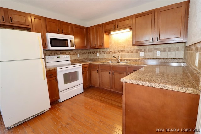 kitchen with light wood-type flooring, white appliances, sink, and backsplash