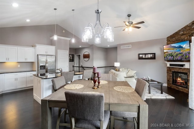 dining room featuring a stone fireplace, ceiling fan with notable chandelier, lofted ceiling, and dark wood-type flooring