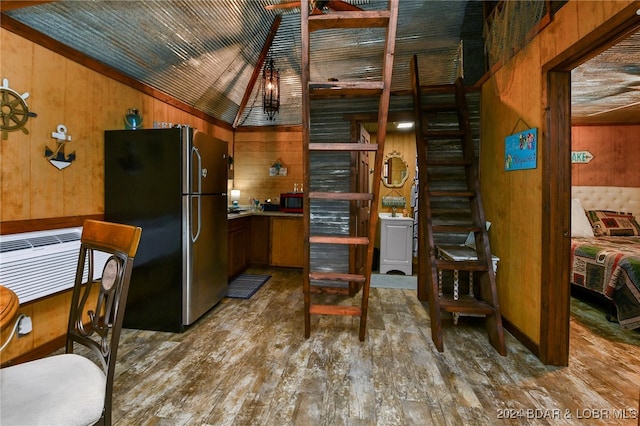 kitchen with wood-type flooring, vaulted ceiling, stainless steel fridge, wood walls, and a wall mounted air conditioner