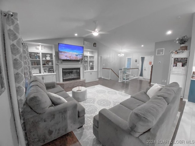 living room with lofted ceiling, built in features, ceiling fan with notable chandelier, and a tile fireplace