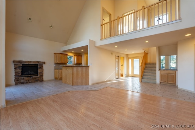 unfurnished living room featuring a stone fireplace, a towering ceiling, and light hardwood / wood-style flooring