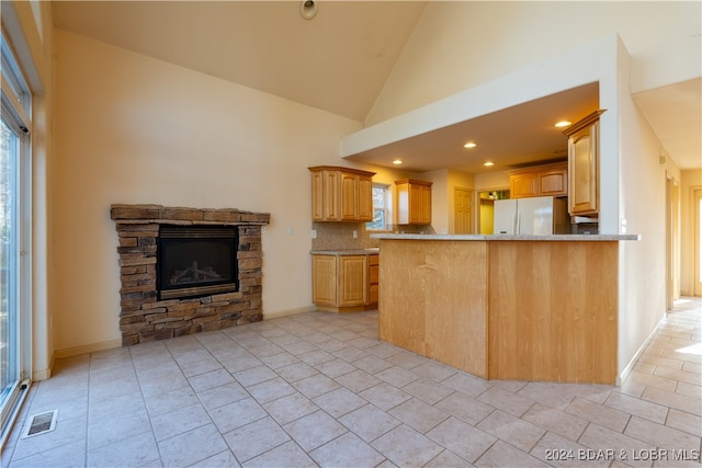 kitchen with light brown cabinetry, high vaulted ceiling, white fridge, and kitchen peninsula