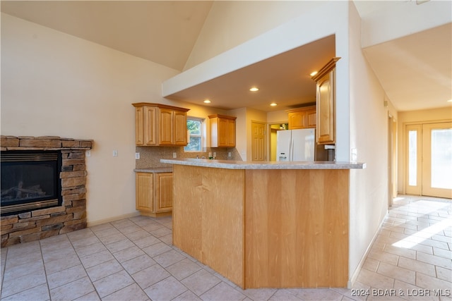 kitchen featuring kitchen peninsula, white fridge with ice dispenser, lofted ceiling, and backsplash