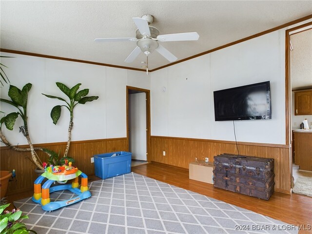 interior space featuring hardwood / wood-style floors, crown molding, ceiling fan, and wood walls