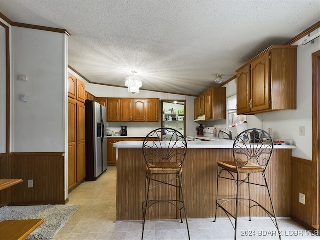 kitchen featuring stainless steel refrigerator with ice dispenser, a breakfast bar area, a textured ceiling, and kitchen peninsula