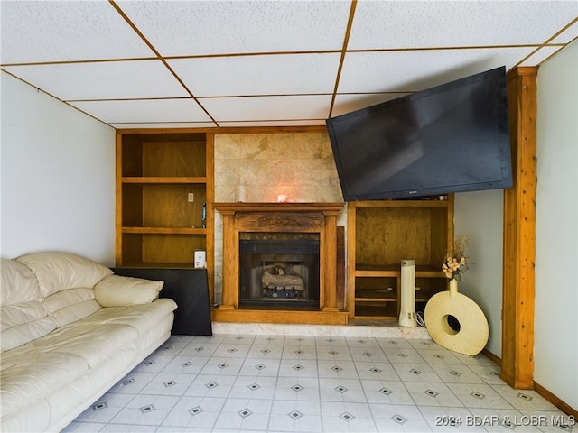 living area with light floors, a fireplace with raised hearth, and a drop ceiling