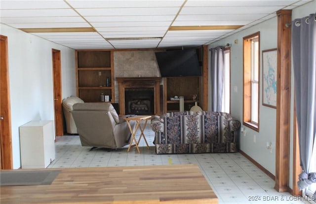 living room with a large fireplace, light floors, a paneled ceiling, and baseboards