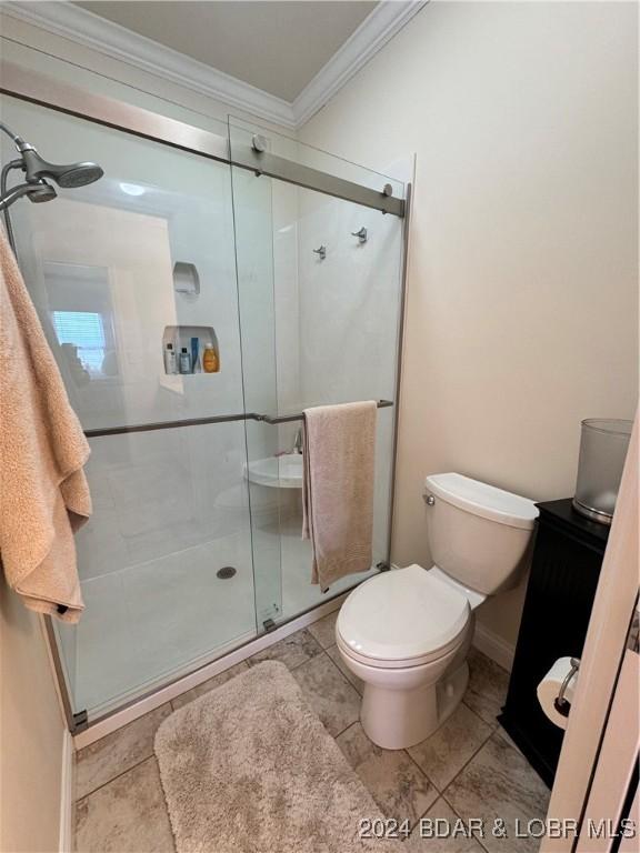 bathroom featuring tile patterned flooring, crown molding, a shower with shower door, and toilet