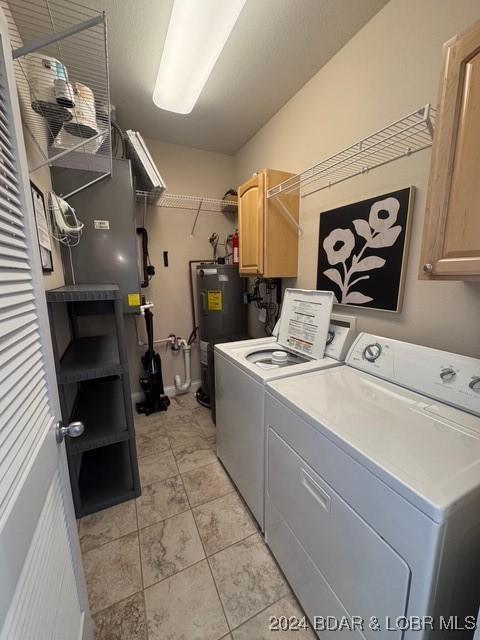 laundry area featuring water heater, washing machine and dryer, and cabinets