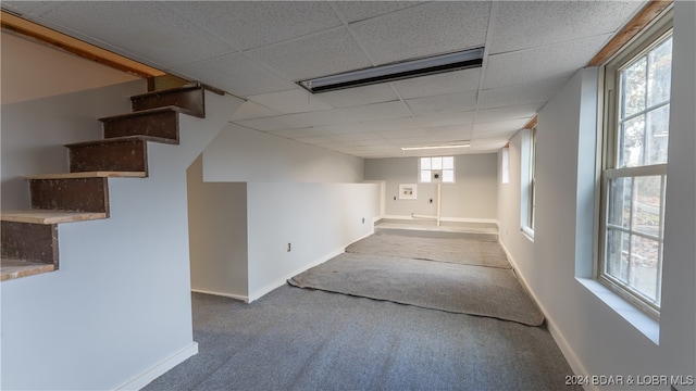 below grade area featuring stairway, carpet flooring, a paneled ceiling, and baseboards