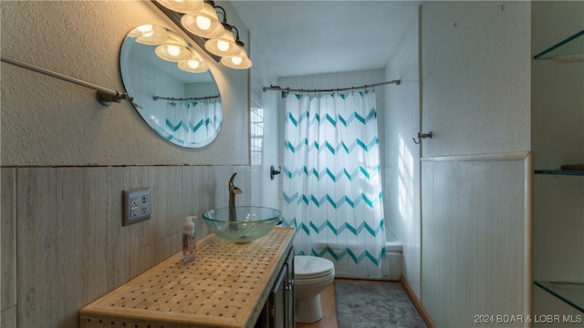 full bathroom with vanity, toilet, wooden walls, and shower / tub combo with curtain