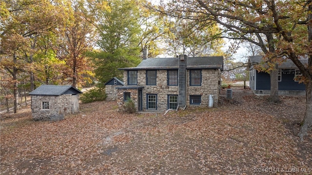 back of house featuring a chimney, a storage unit, central AC, and an outbuilding