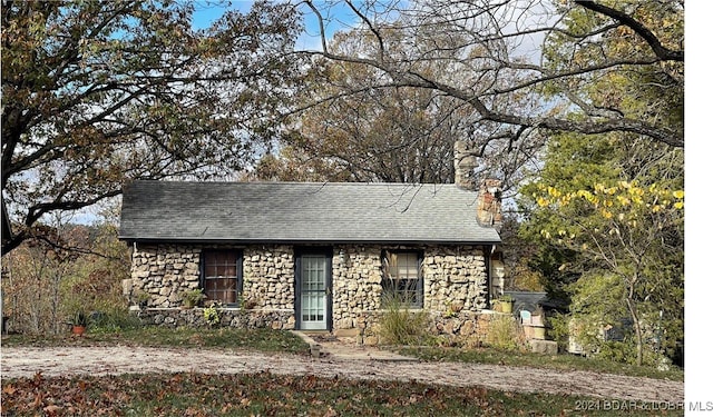 view of front facade with stone siding, roof with shingles, and a chimney