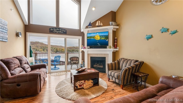 living room featuring a tiled fireplace, high vaulted ceiling, and light hardwood / wood-style flooring