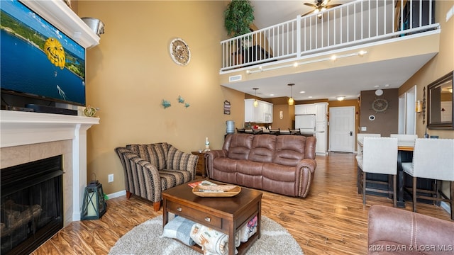 living room featuring a tiled fireplace, ceiling fan, light hardwood / wood-style flooring, and a towering ceiling