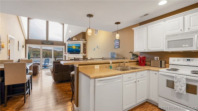 kitchen featuring kitchen peninsula, a kitchen bar, white appliances, sink, and hardwood / wood-style flooring