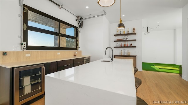 bar with dark brown cabinetry, hanging light fixtures, sink, beverage cooler, and light hardwood / wood-style flooring