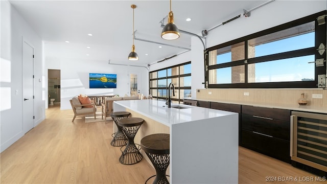 kitchen featuring pendant lighting, sink, an island with sink, light hardwood / wood-style floors, and beverage cooler