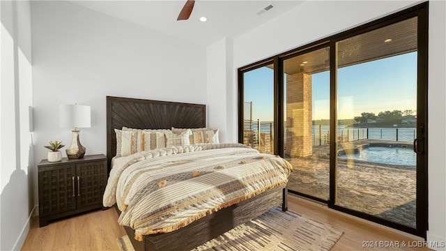 bedroom with access to outside, light hardwood / wood-style floors, a water view, and ceiling fan