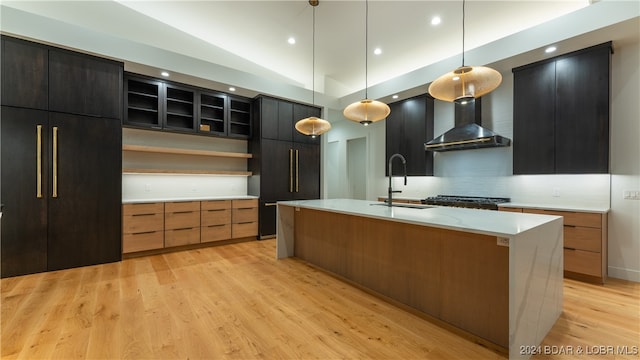 kitchen featuring hanging light fixtures, light hardwood / wood-style floors, wall chimney exhaust hood, and a kitchen island with sink