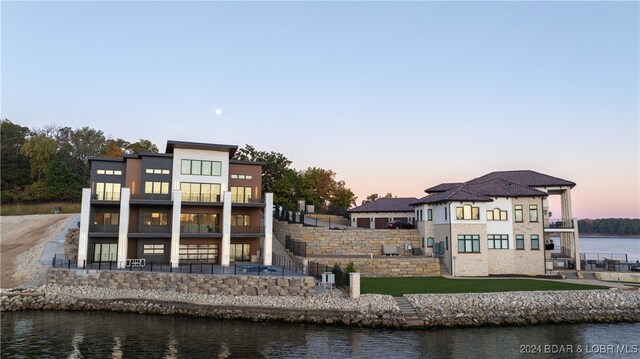 back house at dusk featuring a water view and a balcony