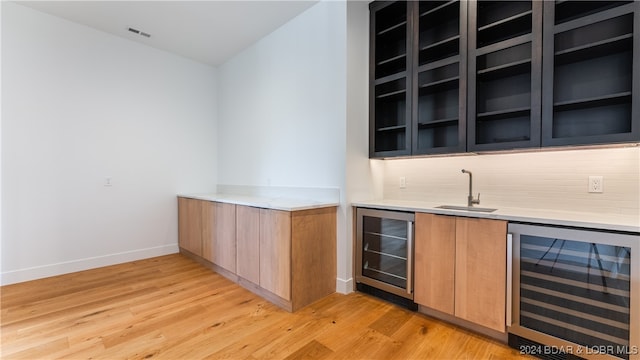 bar with wine cooler, tasteful backsplash, sink, and light hardwood / wood-style flooring